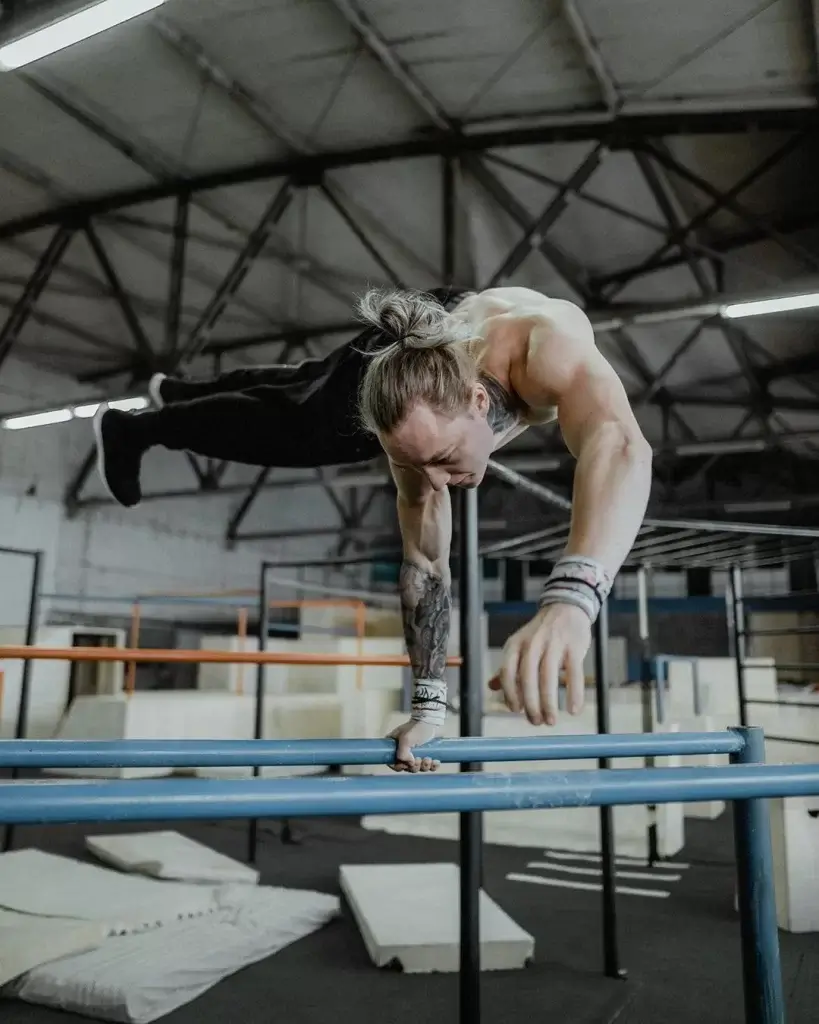 Daniels Laizans haciendo un planche a un brazo en paralelas