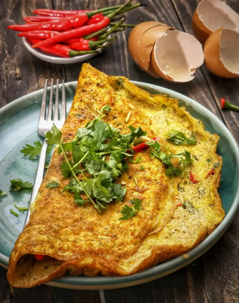 omelette con especias verdes por encima, servido en un plato gris y de fondo unos picantes tabasco y cascaras de huevo