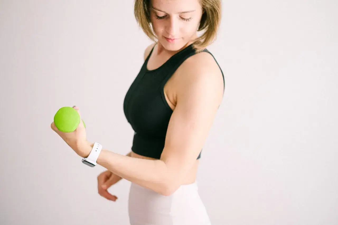 Chica mirandose el bíceps con una manzana verde en la mano